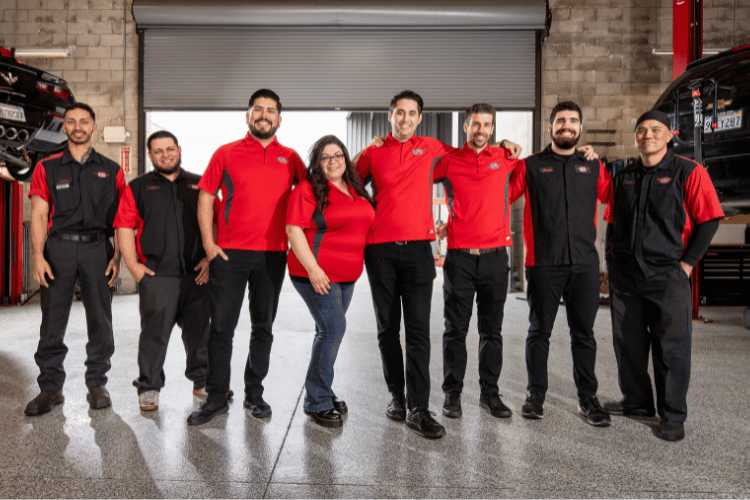 Seven staff members in red and black uniforms standing in front of an industrial garage door