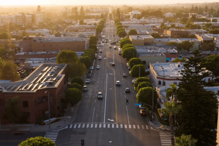 Aerial view of a city street at sunset with cars, trees, and buildings on both sides