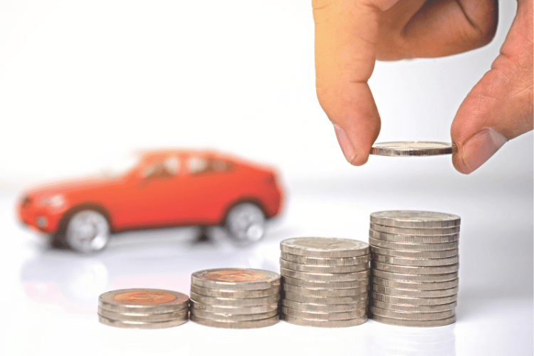 Hand placing a coin above stacked coins with a red toy car in the background