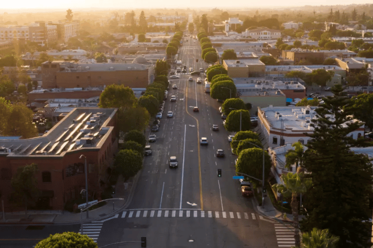 Aerial view of a sunlit city street with trees, cars, and buildings at sunset