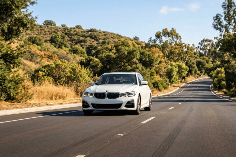 White BMW sedan driving along a scenic road, highlighting fall car care