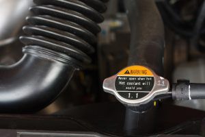 Close-up of a car radiator cap with a warning label and black hoses in the engine bay