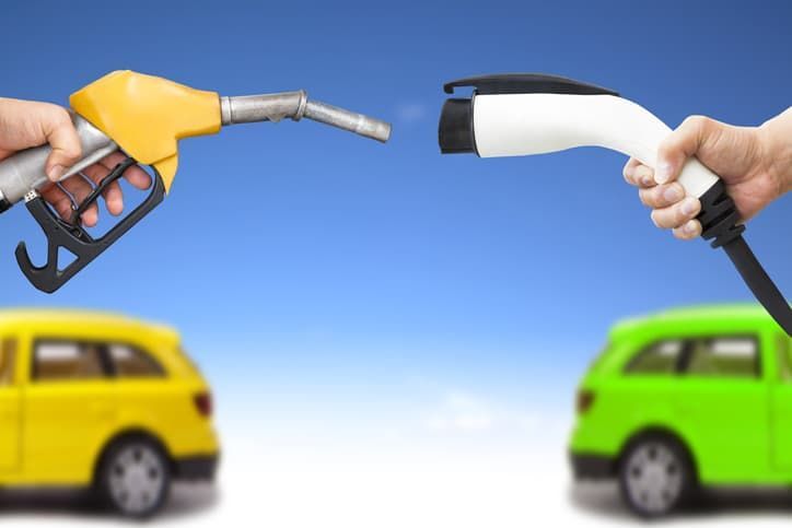 Hands holding fuel nozzles near yellow and green cars, symbolizing a cleaner fuel choice.