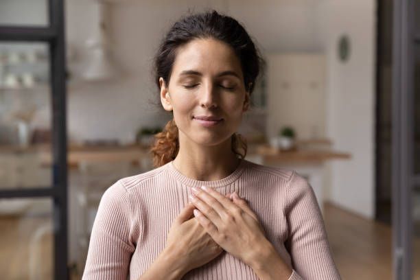 Woman with eyes closed and hands on chest, indoors. She appears calm and at peace.