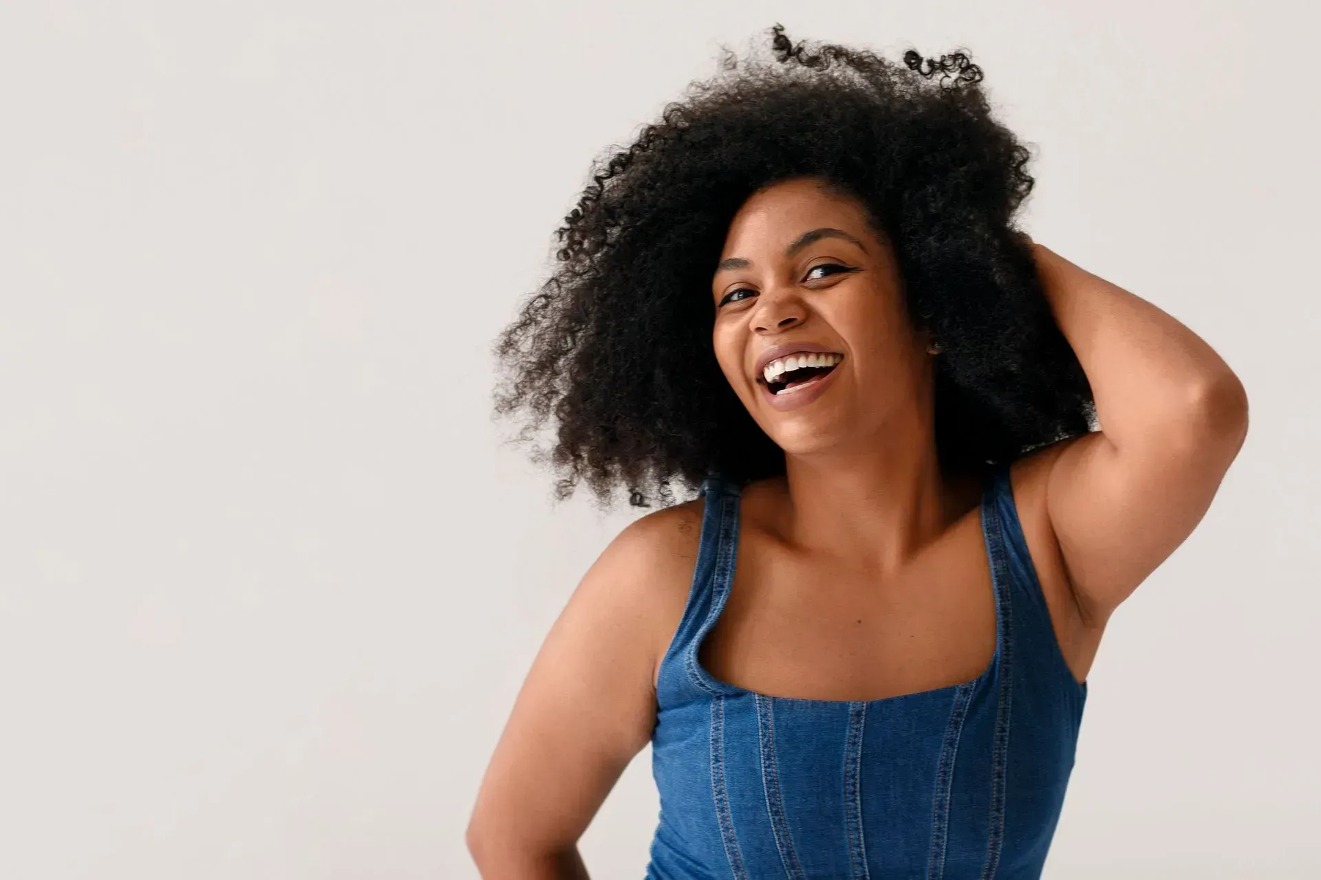 Woman smiling with dark curly hair, wearing a blue top, hand in hair.