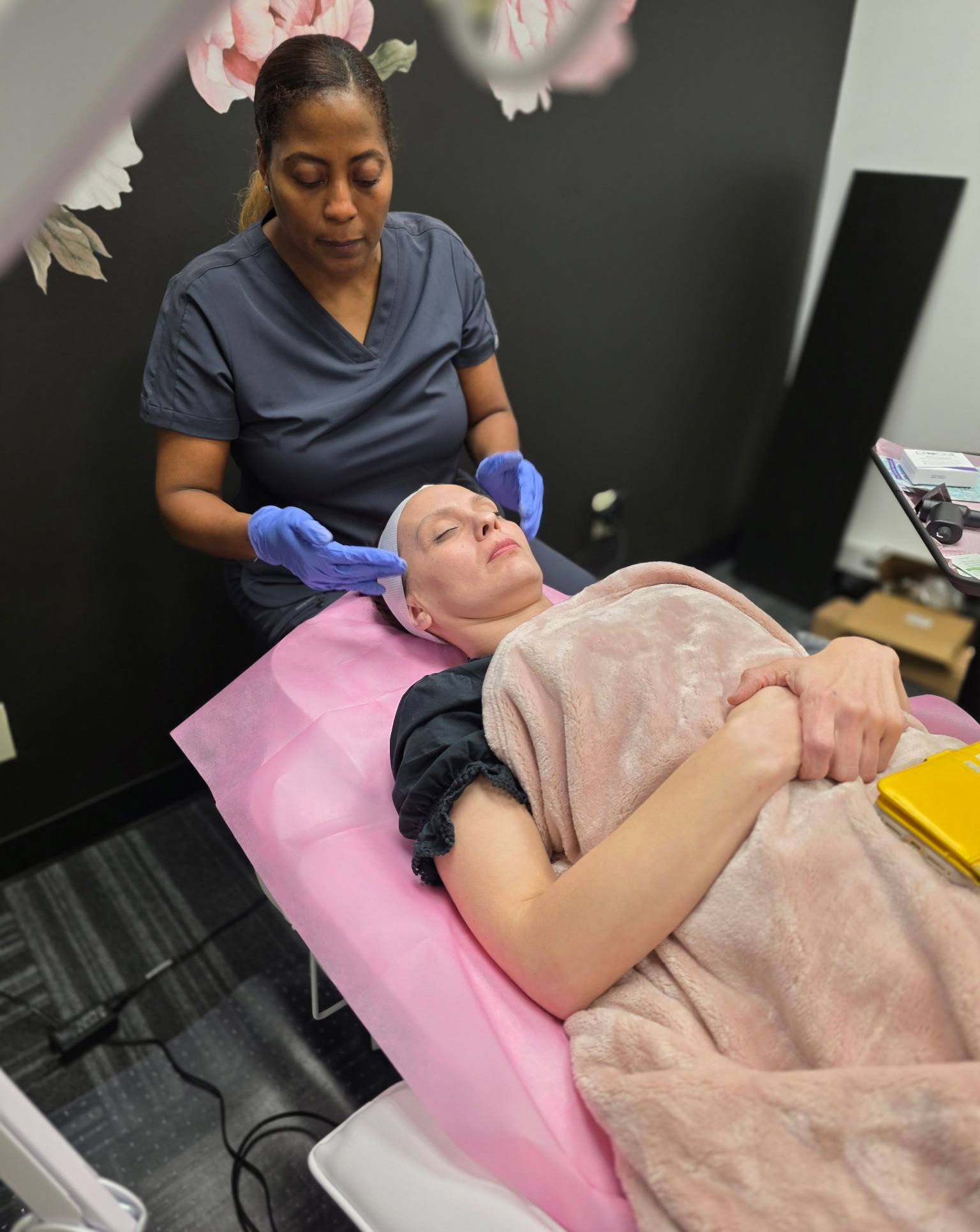 Woman receiving facial treatment from a person wearing blue gloves, in a beauty studio.