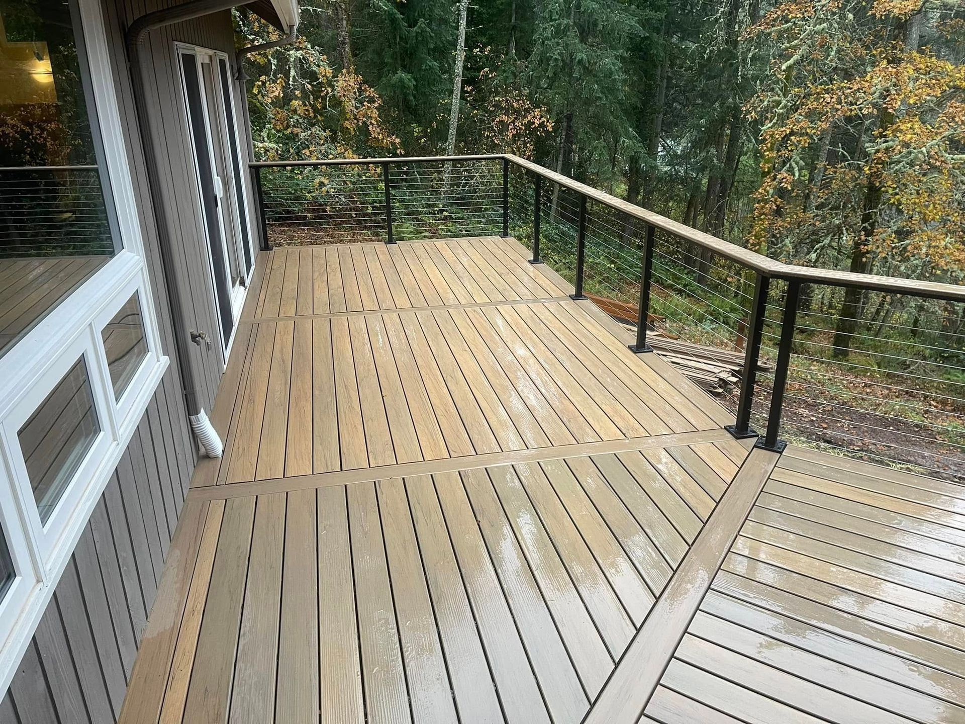 Wooden deck with black railings overlooking a wooded area. The deck is wet.