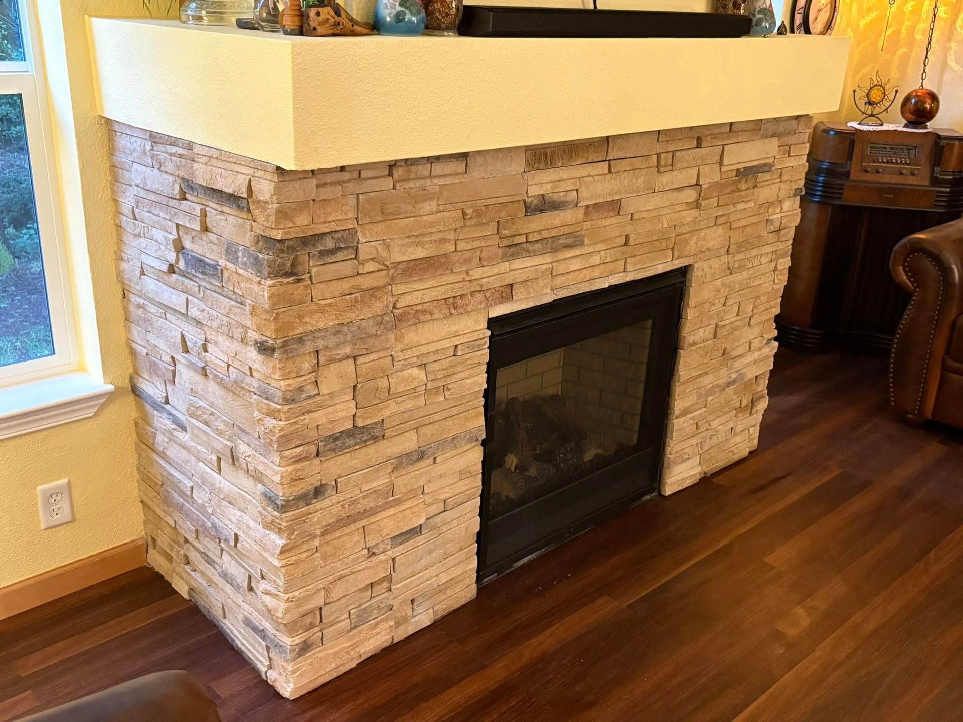 Fireplace with beige stone facade, a black firebox, and a cream-colored mantle.