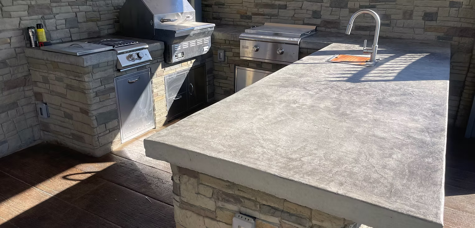 Outdoor kitchen with grill, sink, and countertop built into a stone structure.