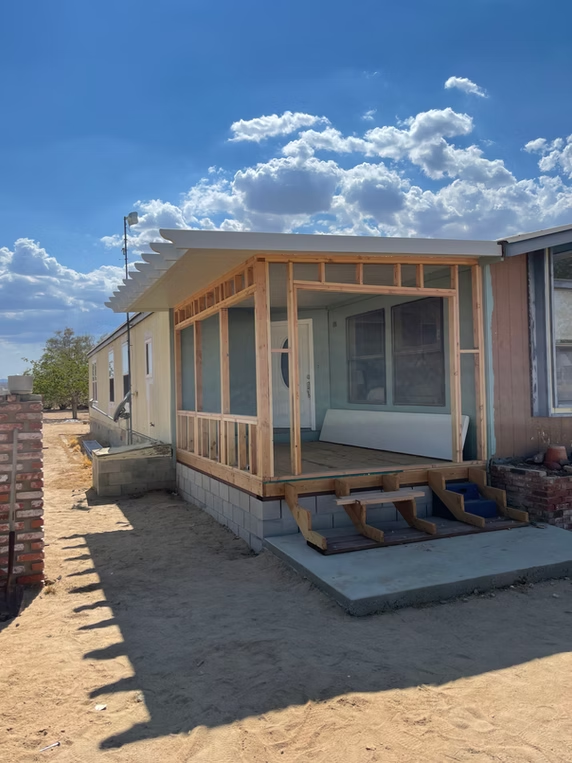 A mobile home with a new wooden porch under construction, on a sunny day.