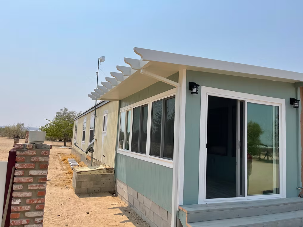 A light blue house with a white pergola, large sliding glass door, and a brick wall next to it.