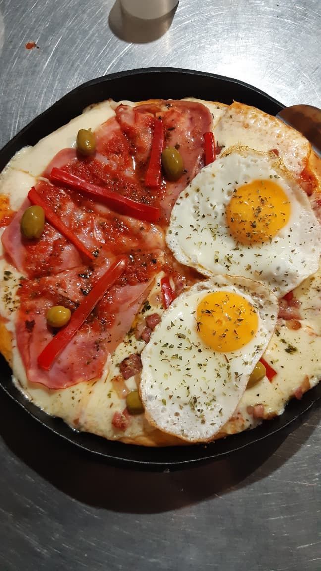 Pizza con jamón, pimientos rojos, aceitunas y dos huevos fritos en una sartén de hierro fundido.