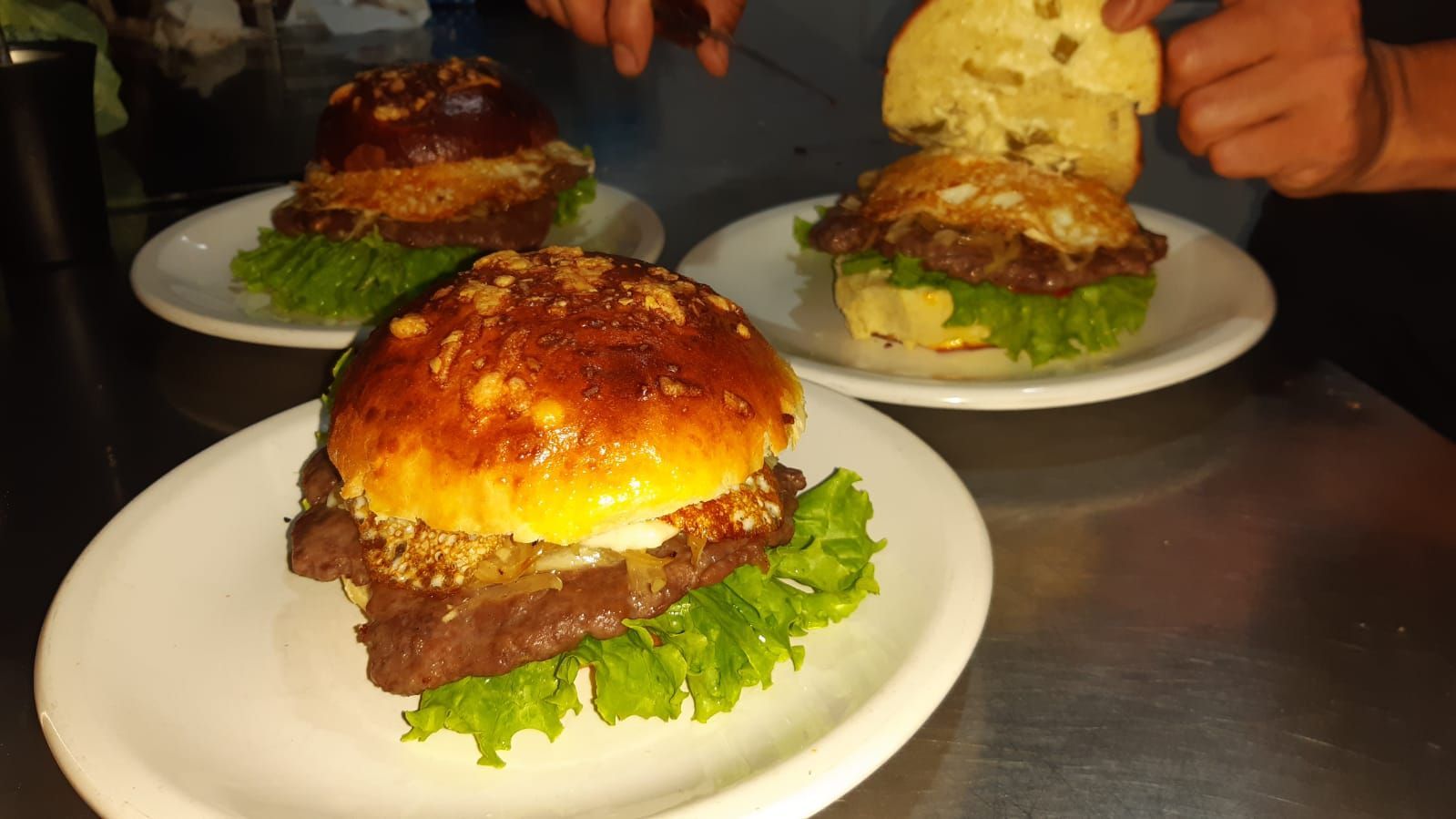 Tres hamburguesas gourmet en platos con lechuga; a una de ellas se le agrega un panecillo encima.