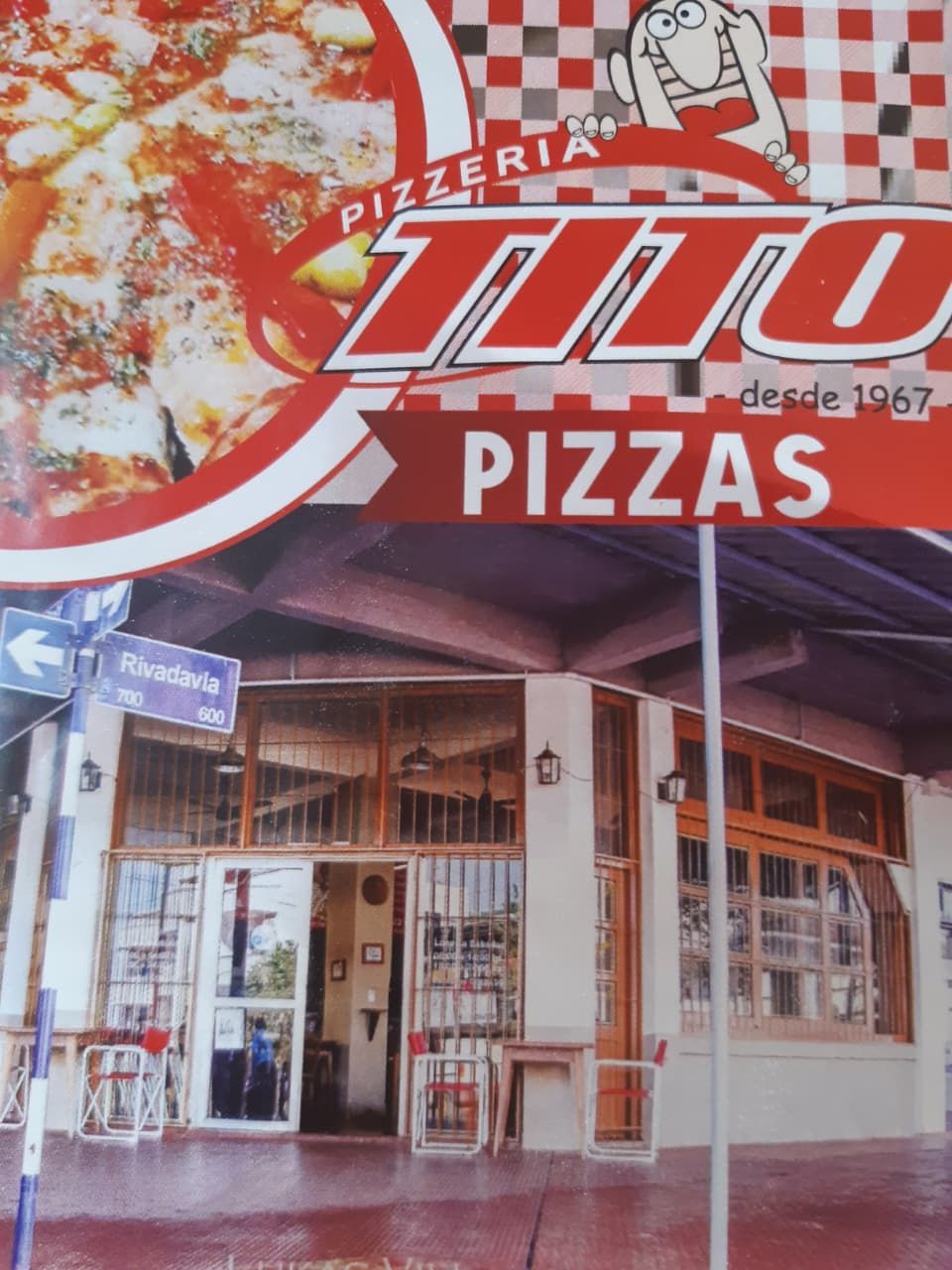 Exterior de Pizzeria Tito, con logo rojo y blanco; edificio con ventanas y puertas abiertas.