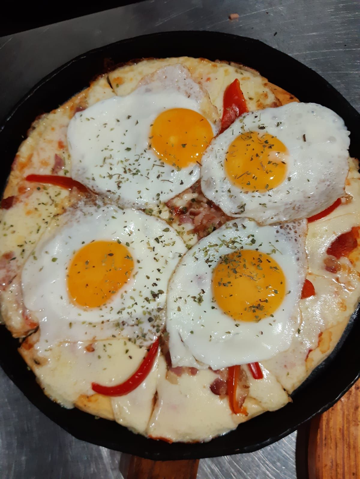 Pizza cubierta con cuatro huevos fritos, queso y pimientos rojos en una sartén negra.