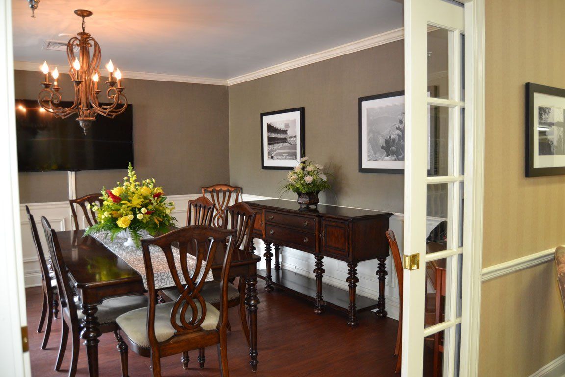 A dining room with a long table and chairs and a flat screen tv.