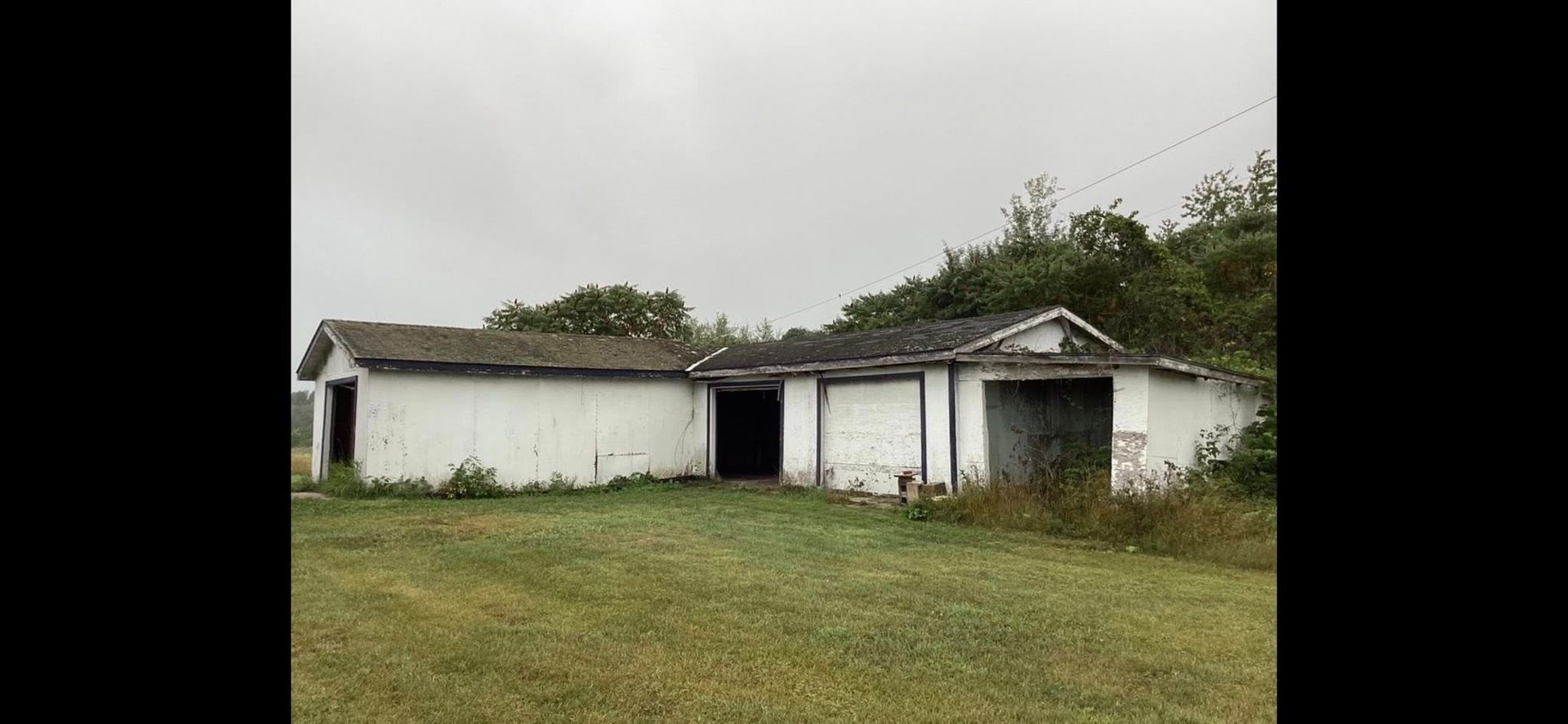 Old white house with a gray roof on a grassy lot under an overcast sky