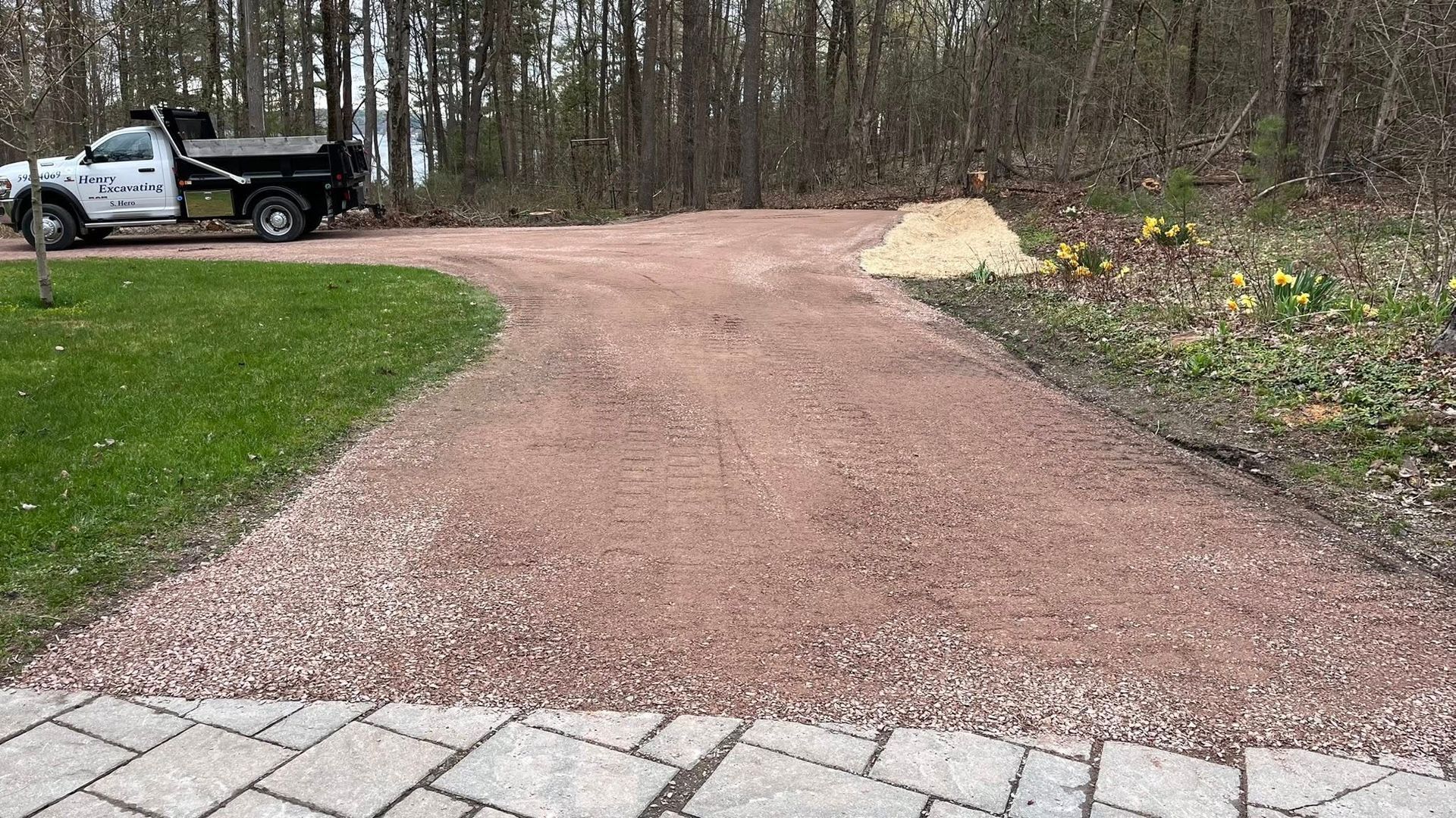 Gravel driveway under construction beside a parked truck, with a sand pile and paving stones in front.