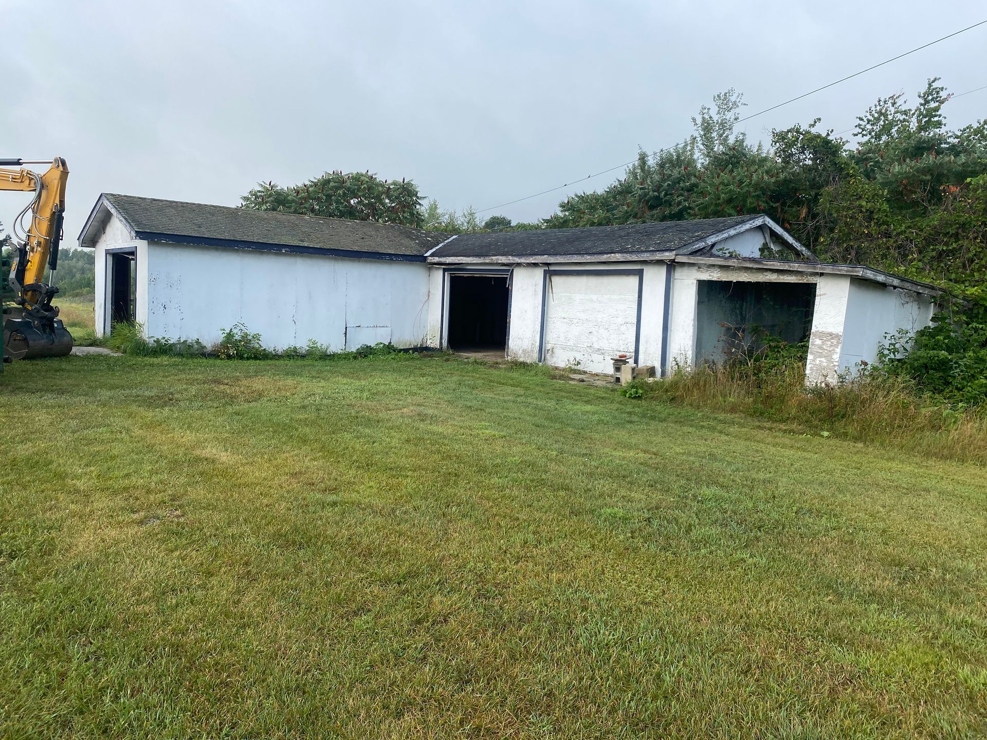 Old white farm shed with a dark open doorway, set in a grassy yard under a cloudy sky.