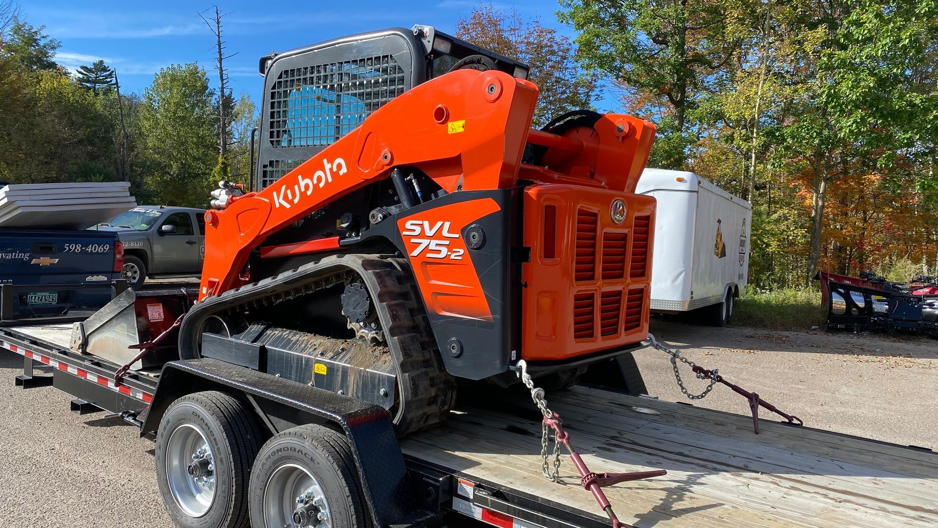 Orange Kubota SVL75 track loader strapped to a flatbed trailer outdoors under a blue sky.