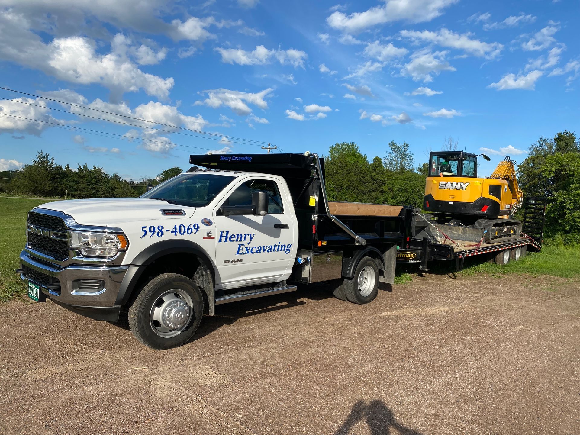 Tow truck hauling a yellow excavator on a flatbed trailer under a blue sky.