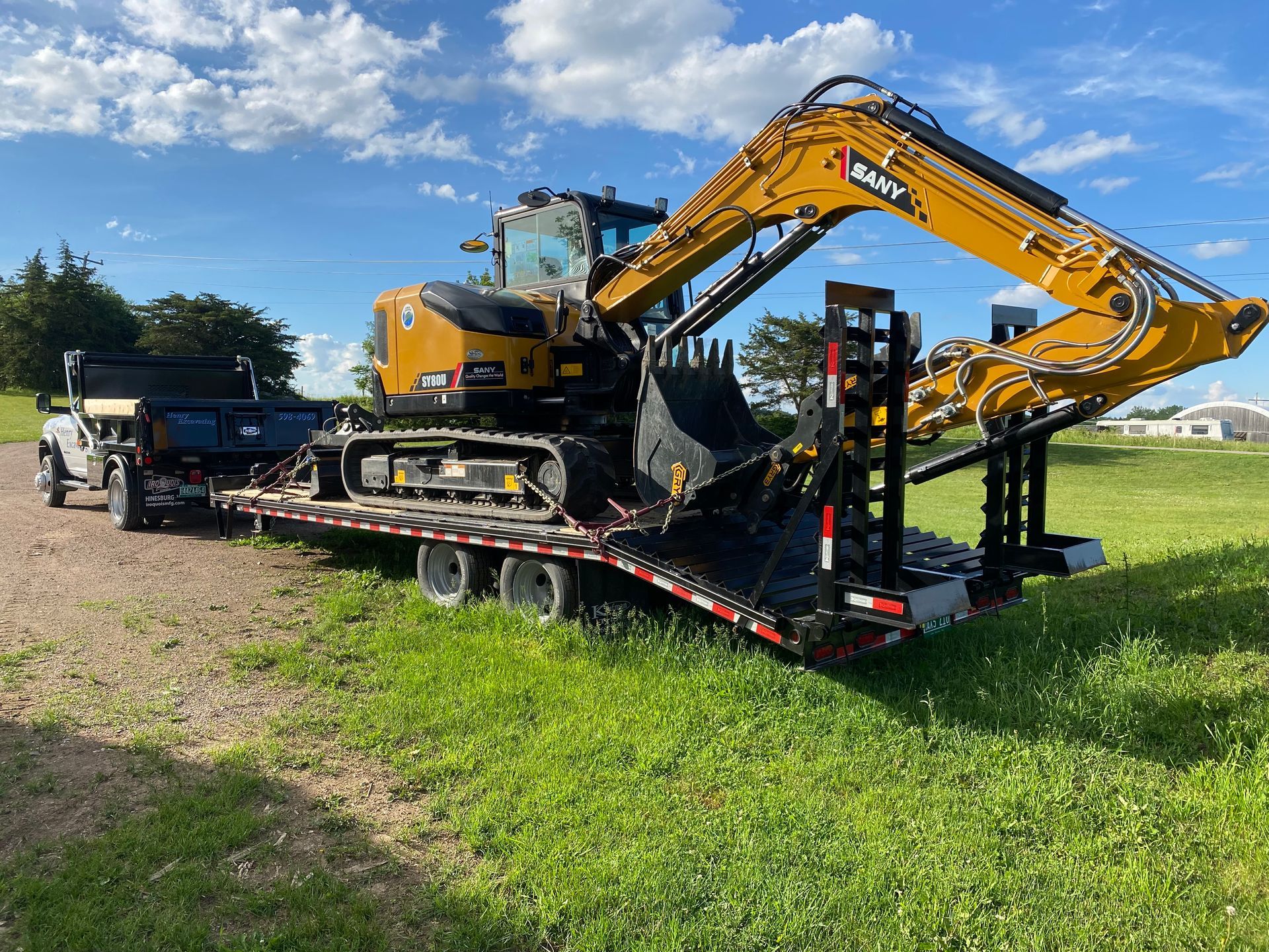 Yellow excavator loaded on a flatbed trailer in a grassy field under a blue sky