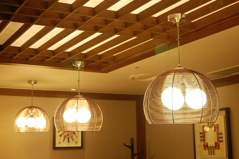 Three globe-shaped pendant lights with glowing bulbs hang from the ceiling. Woven basket shades. Wooden grid ceiling.