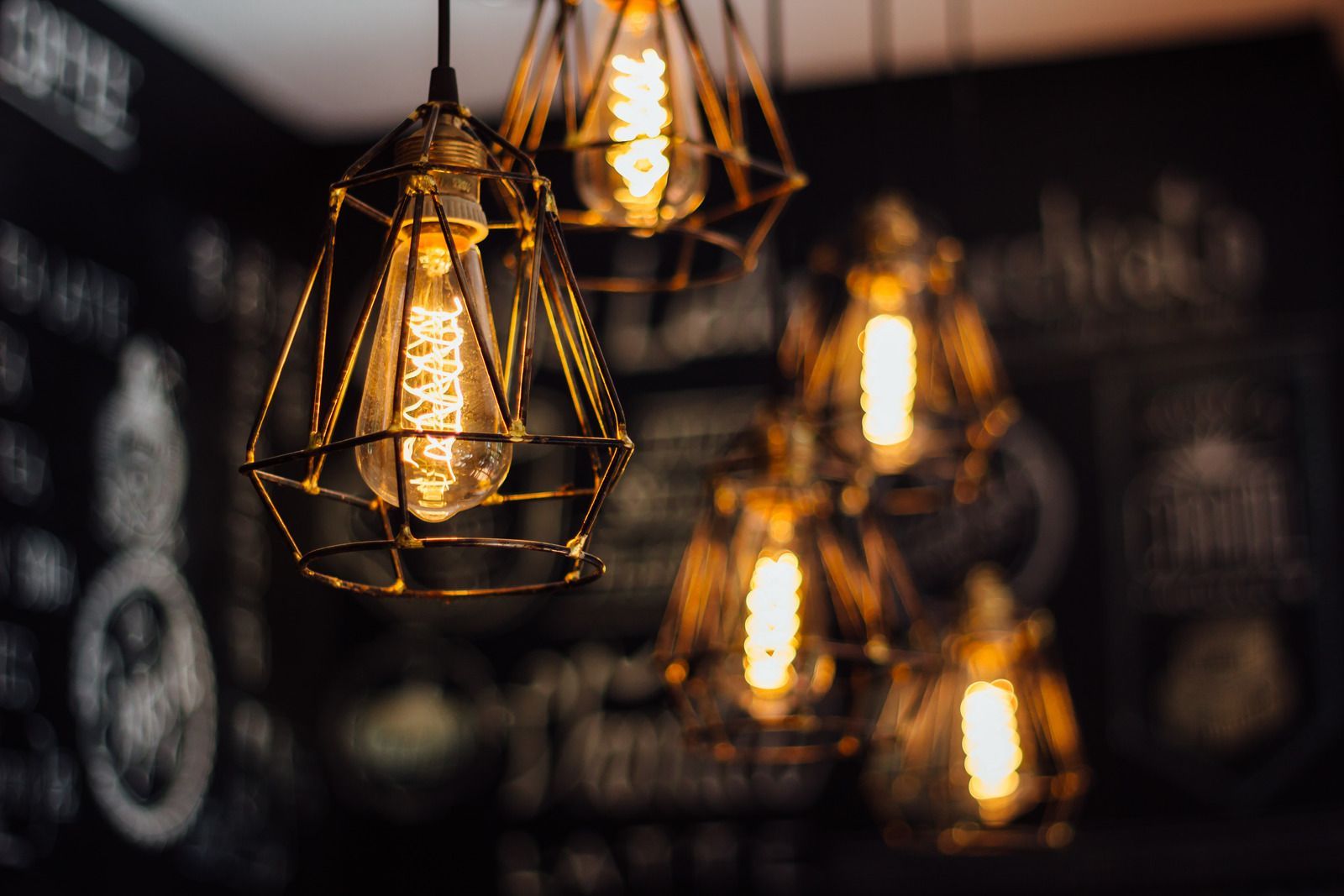 Geometric pendant lights with warm, glowing Edison bulbs against a dark background.