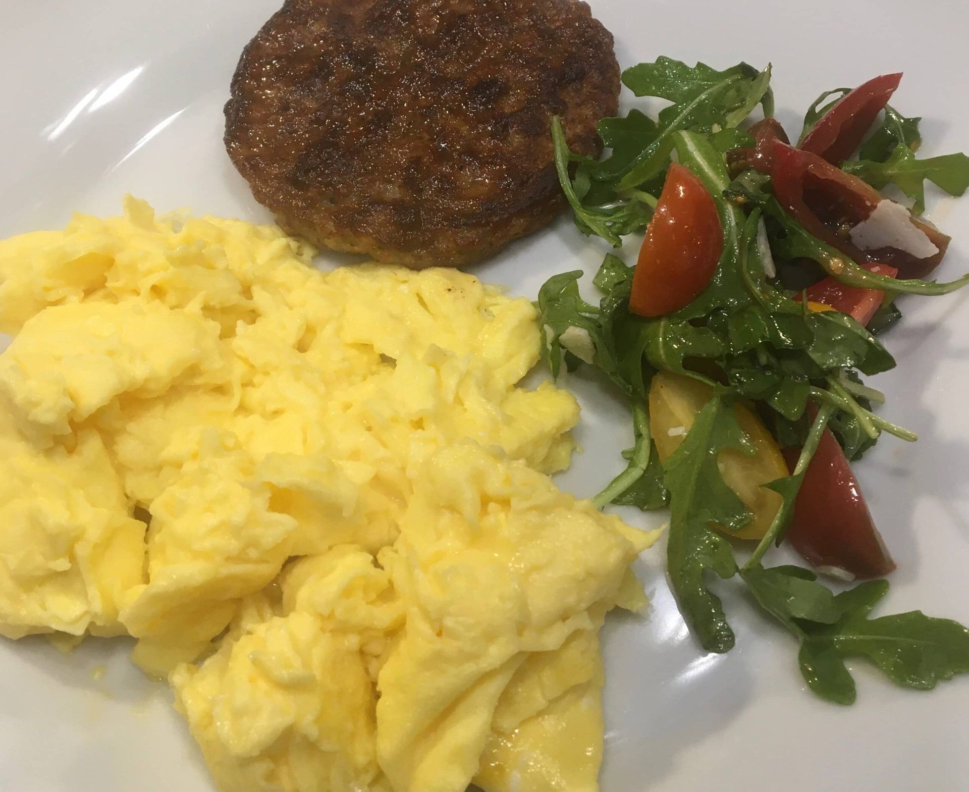 A white plate topped with scrambled eggs a salad and a sausage patty