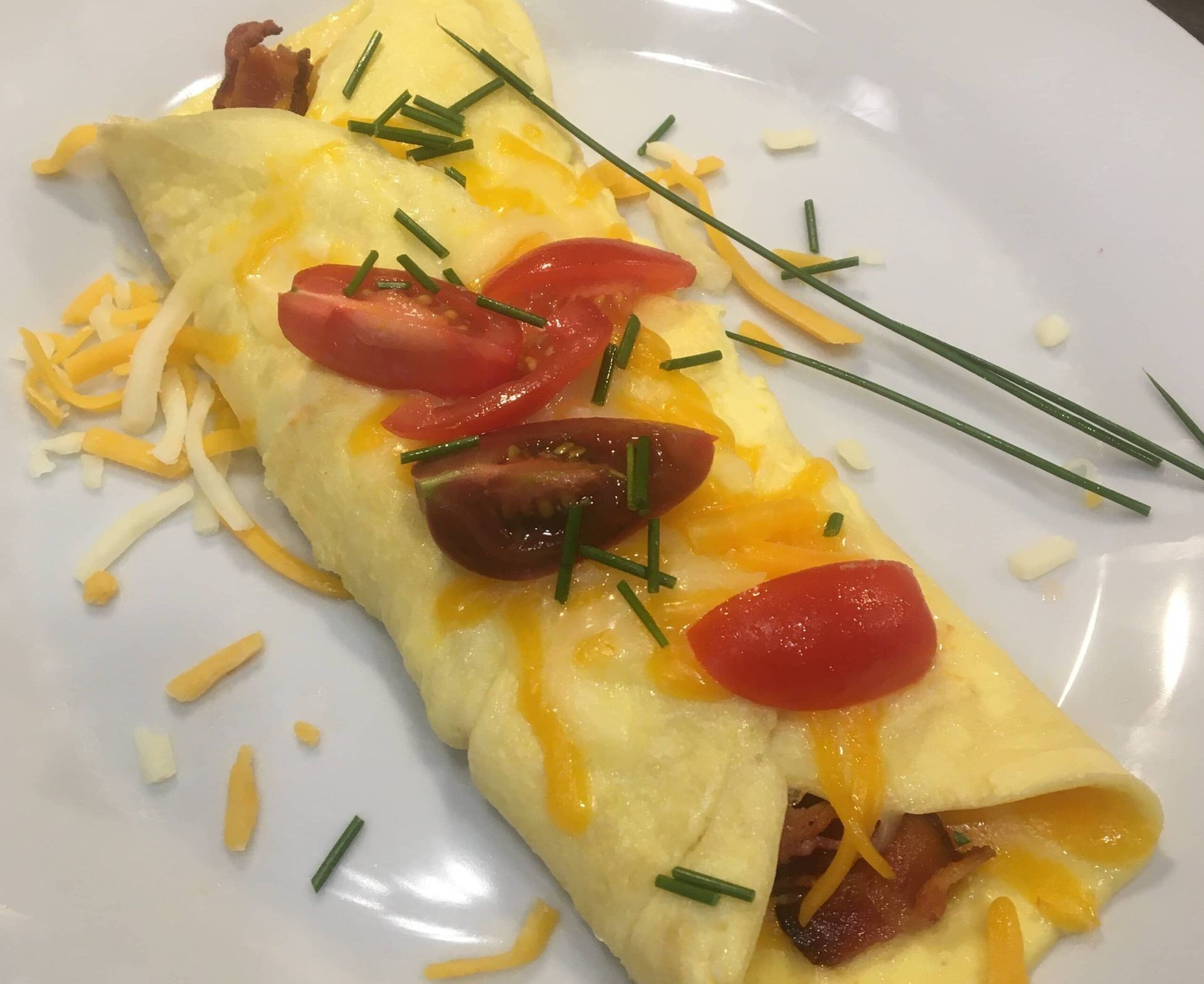 A white plate topped with an omelet with cheese tomatoes and bacon