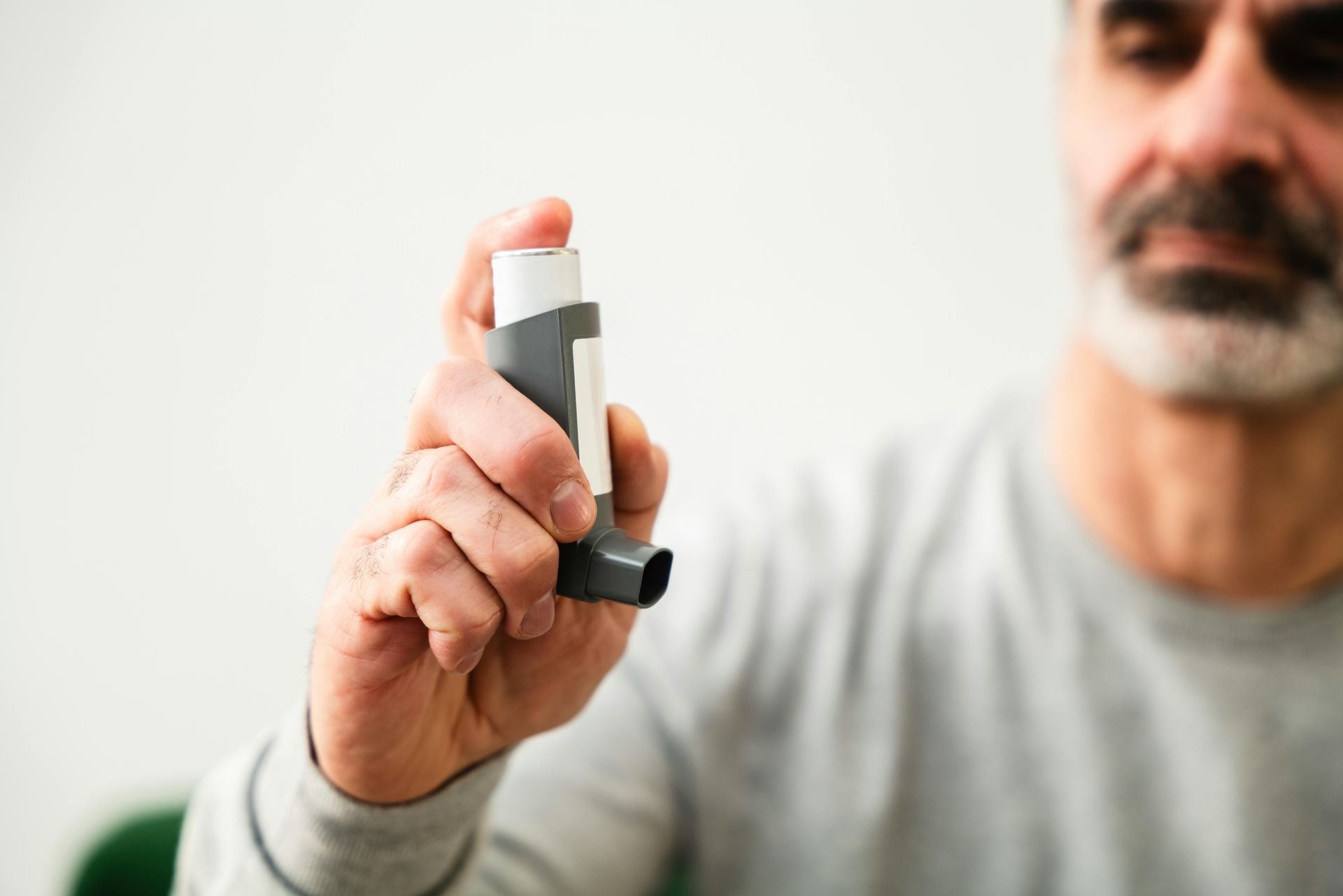 Person holding a gray inhaler near their face against a blurred white background