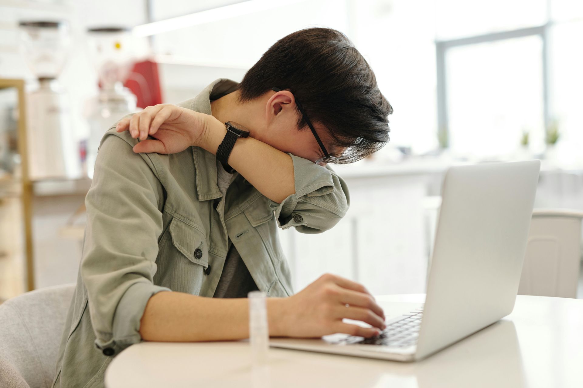 Person at desk with laptop, head in hand, appearing tired or stressed.