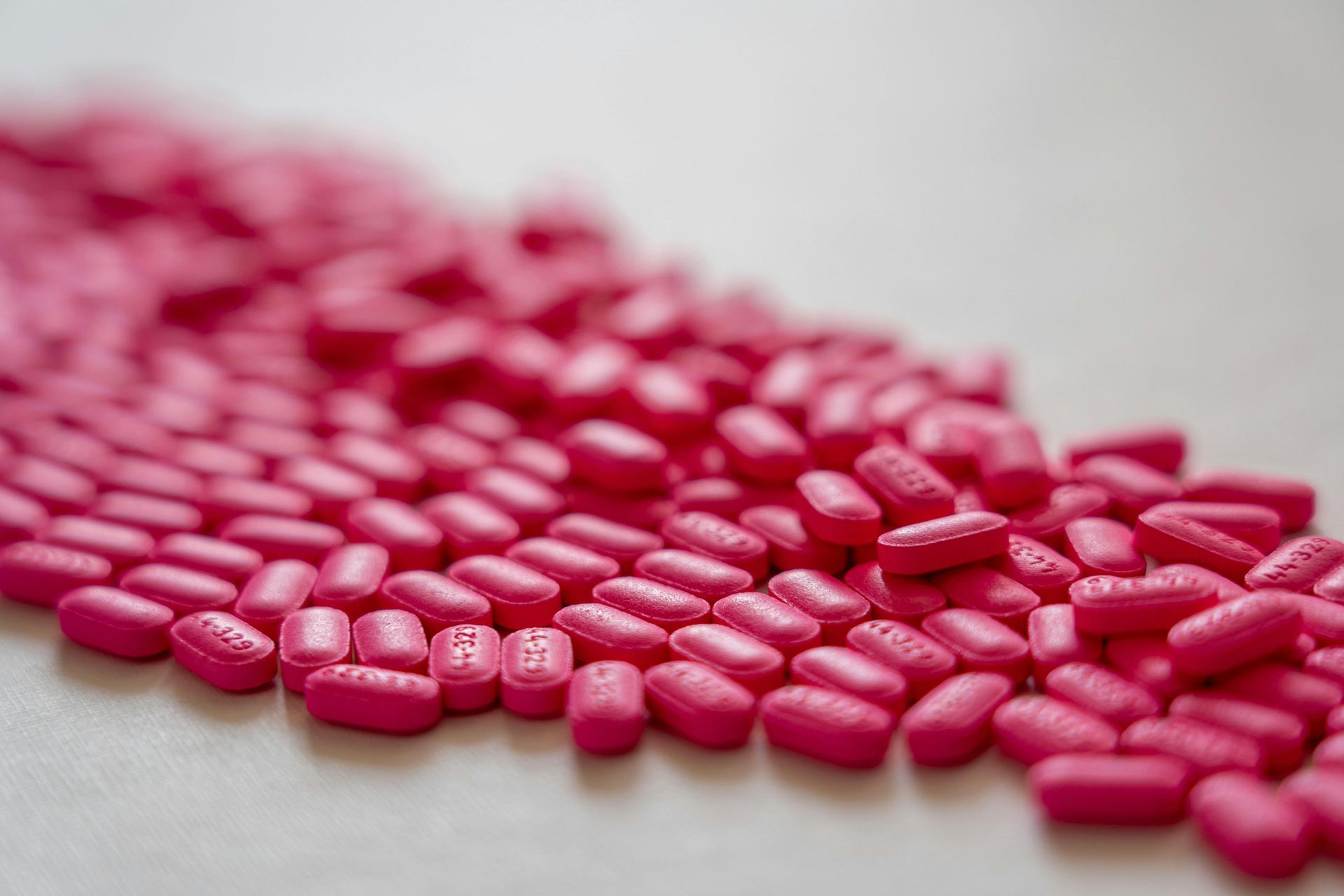 Pile of pink oblong pills scattered on a white surface