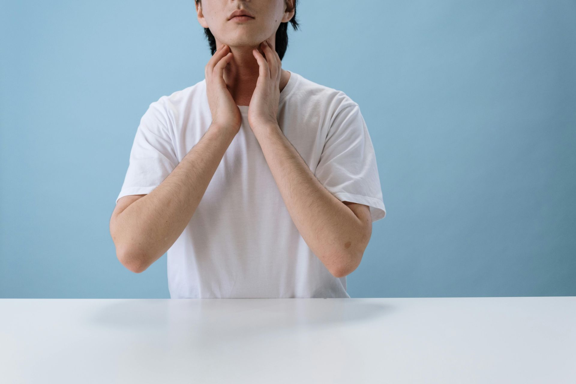 Person in a white shirt holding their neck against a light blue background