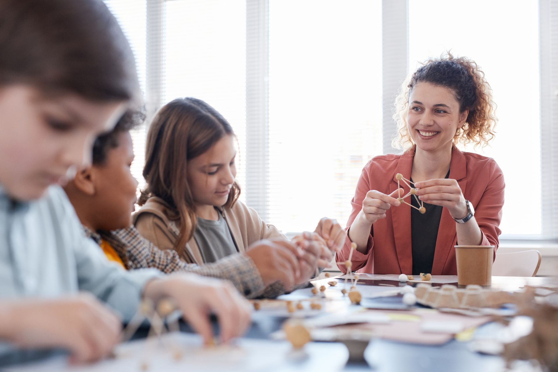People collaborating at a table, with a smiling woman in a red cardigan speaking and holding a phone.