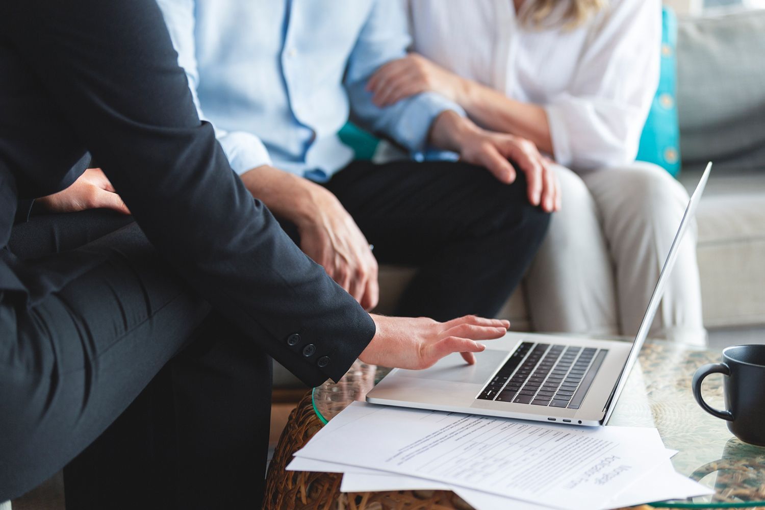 A person in a suit points to a laptop screen, showing a document to an embracing couple.