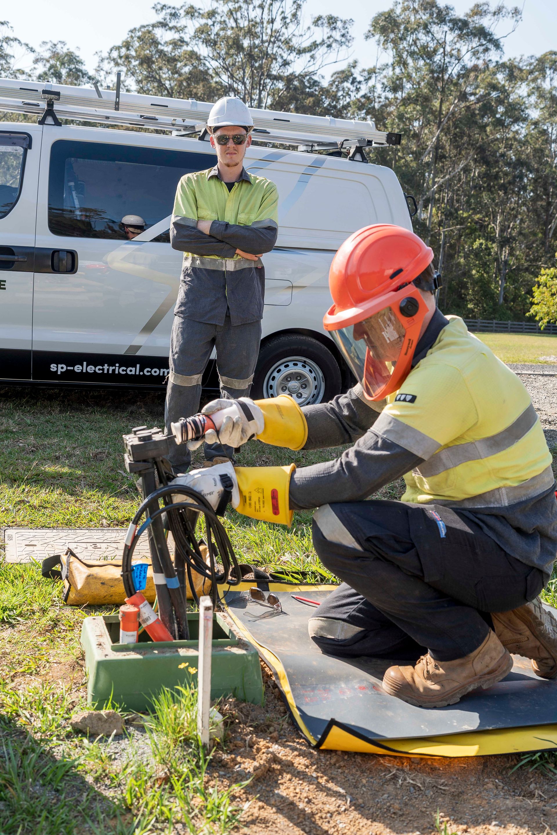 Electrician in orange helmet working on equipment; another stands by the van — Stuart Pearce Electrical In NSW Urunga, NSW