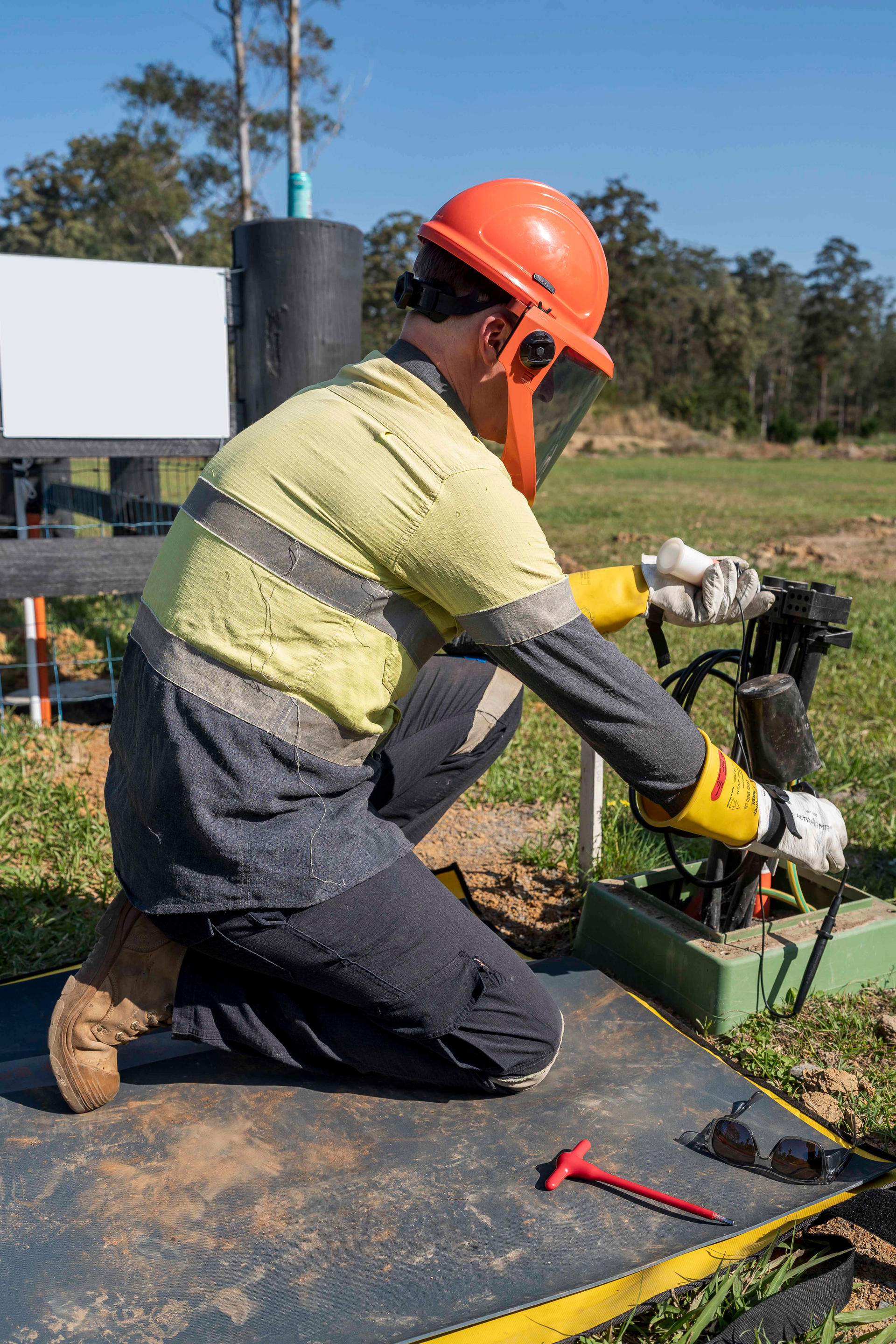 Worker in safety gear kneeling, working on equipment outdoors — Stuart Pearce Electrical In NSW Coffs Harbour, NSW