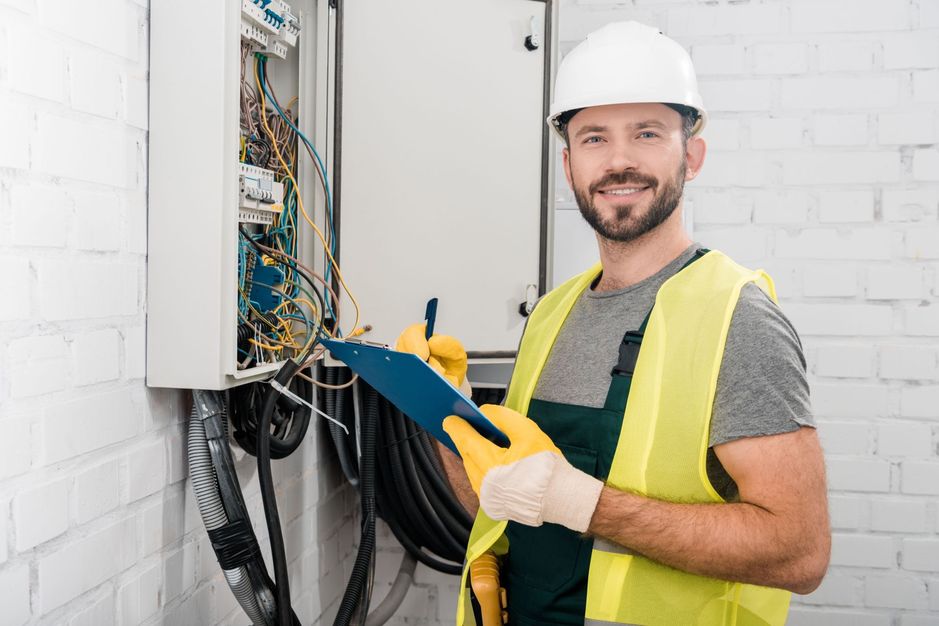 a man in a hard hat is holding a clipboard in front of an electrical box .