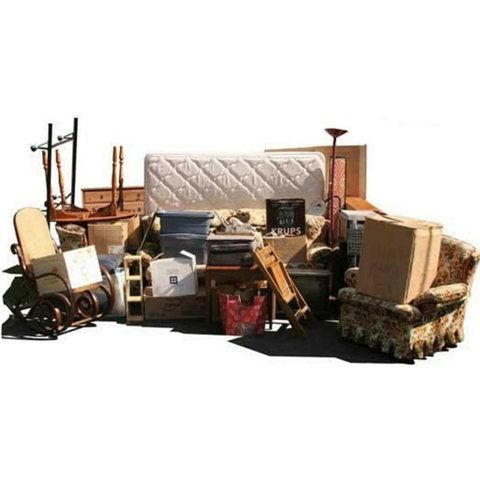 Assorted old furniture and household items piled in a cluttered room against a white wall.