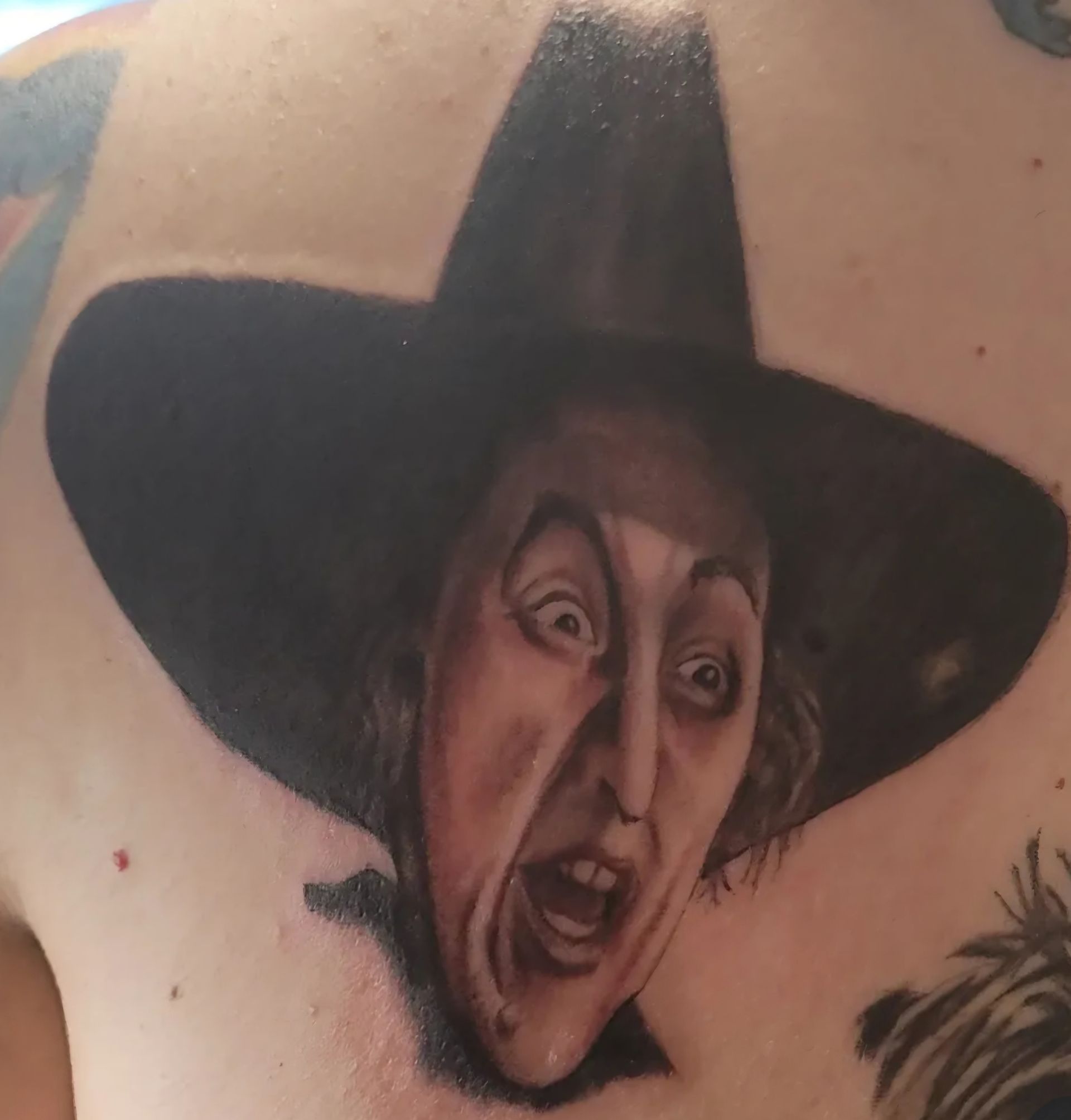 A tattoo of the Wicked Witch of the West from The Wizard of Oz, wearing her hat, with a screaming expression.