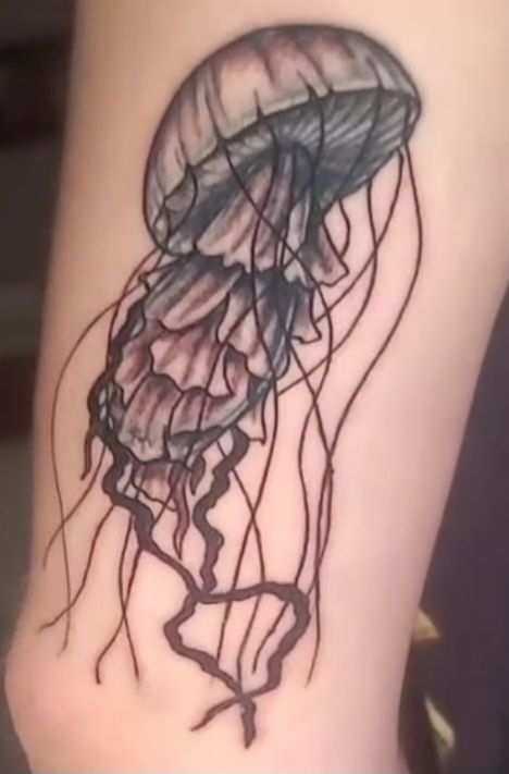 Black and gray jellyfish tattoo on skin, detailed shading with flowing tentacles.