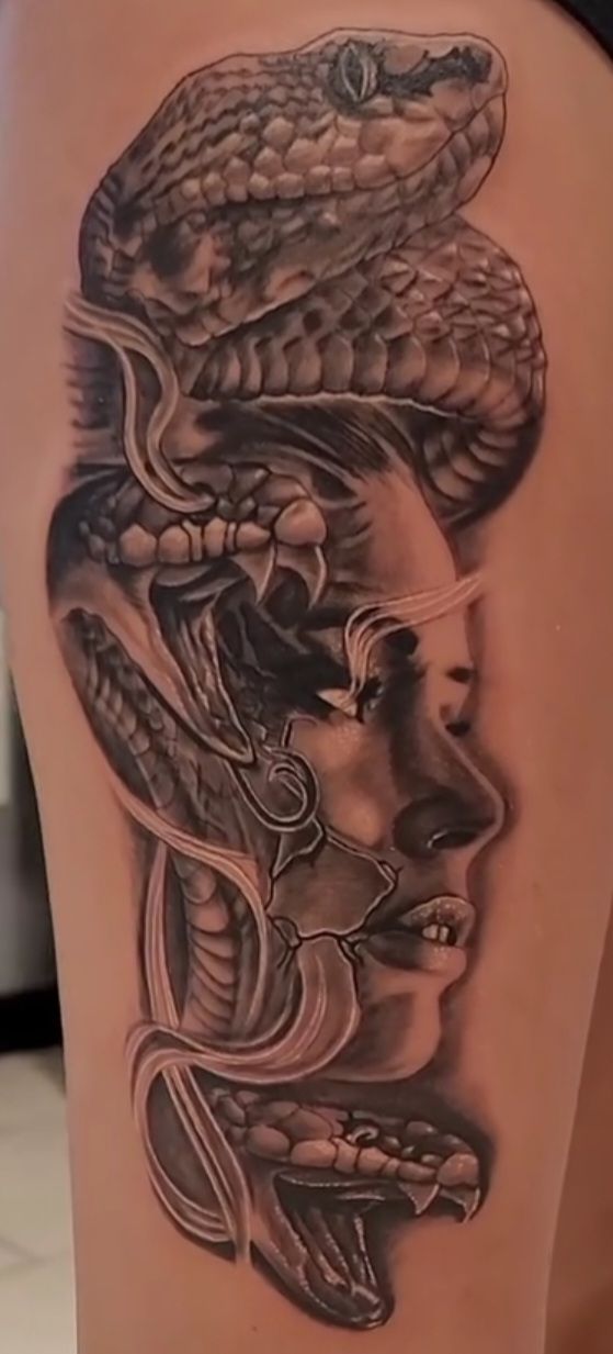 Tattoo of a woman's face with a snake coiled around it. Black and gray shading on thigh.