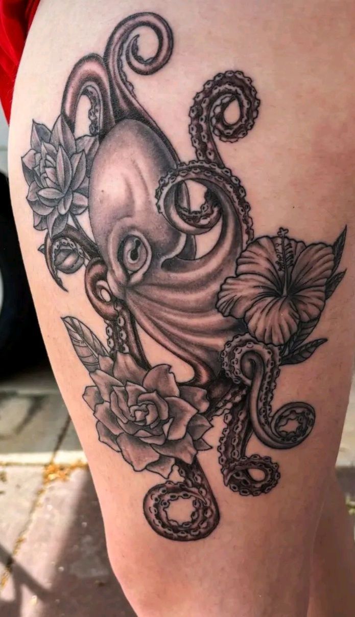 Tattoo of an octopus with surrounding flowers on a person's thigh. In black and gray shading.