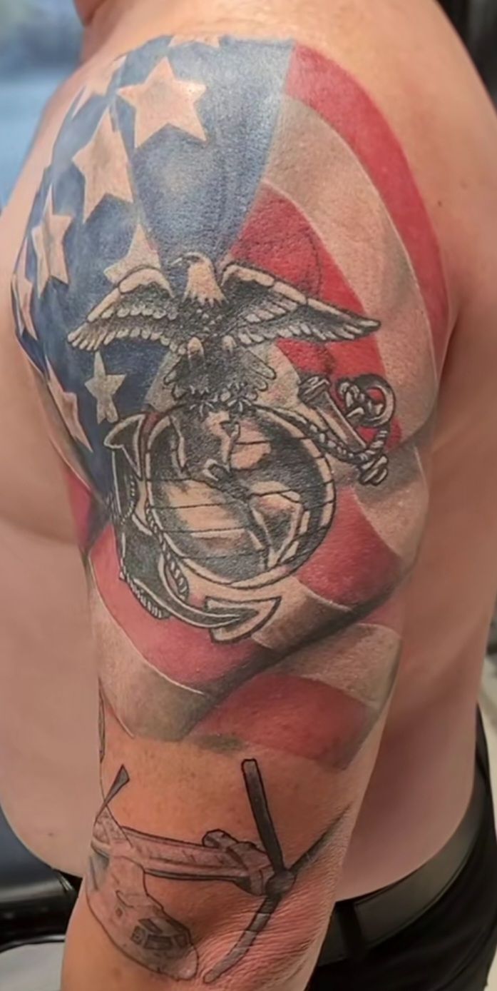 Tattoo of US flag and Marine Corps emblem on a man's arm. Includes an eagle and a helicopter.