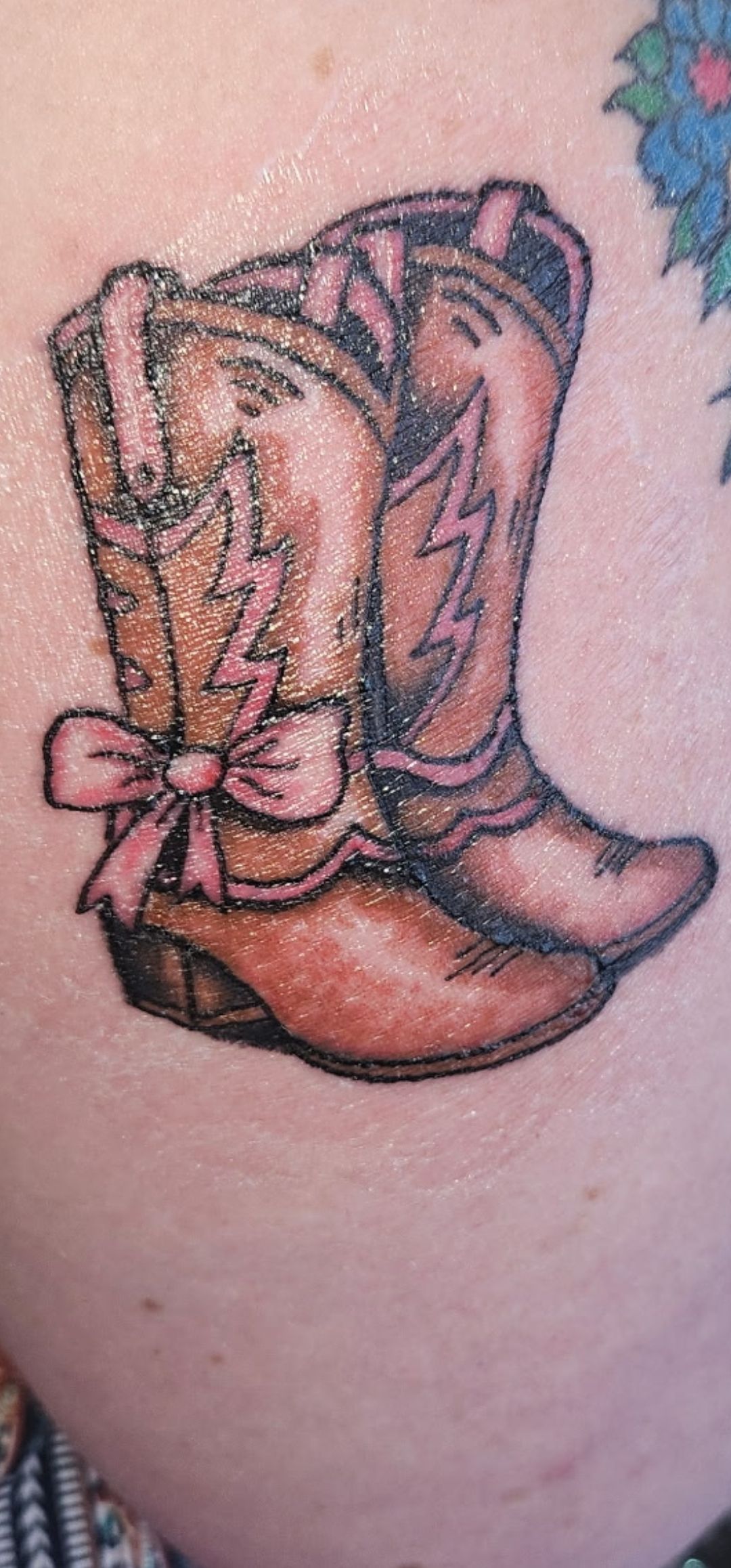 Brown cowboy boots tattoo on skin, decorated with pink flowers and star accents