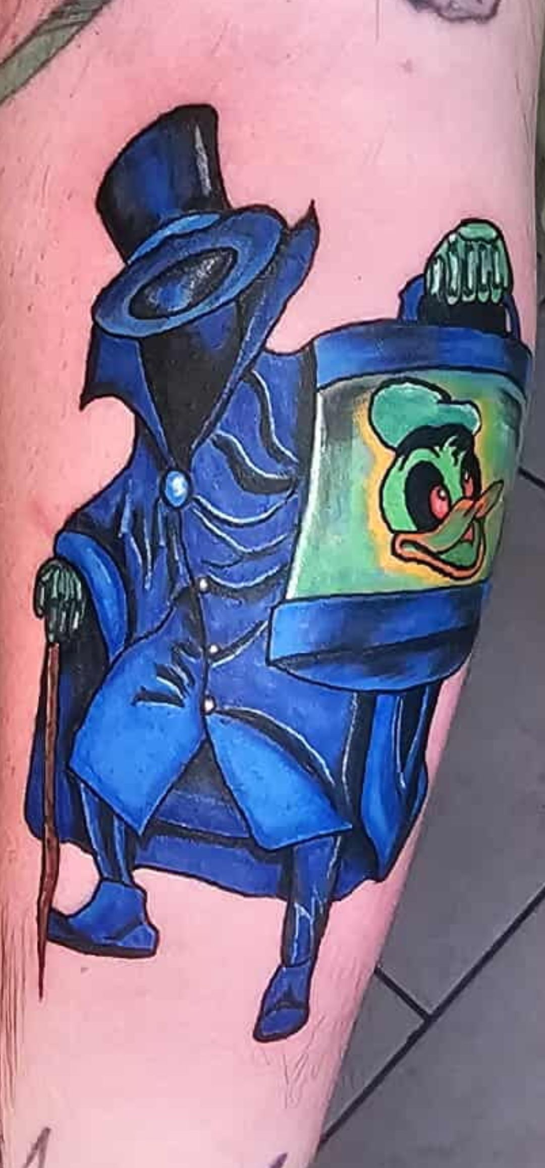 Colorful blue backpack-style tattoo with a cartoon face and green bottle on pink skin