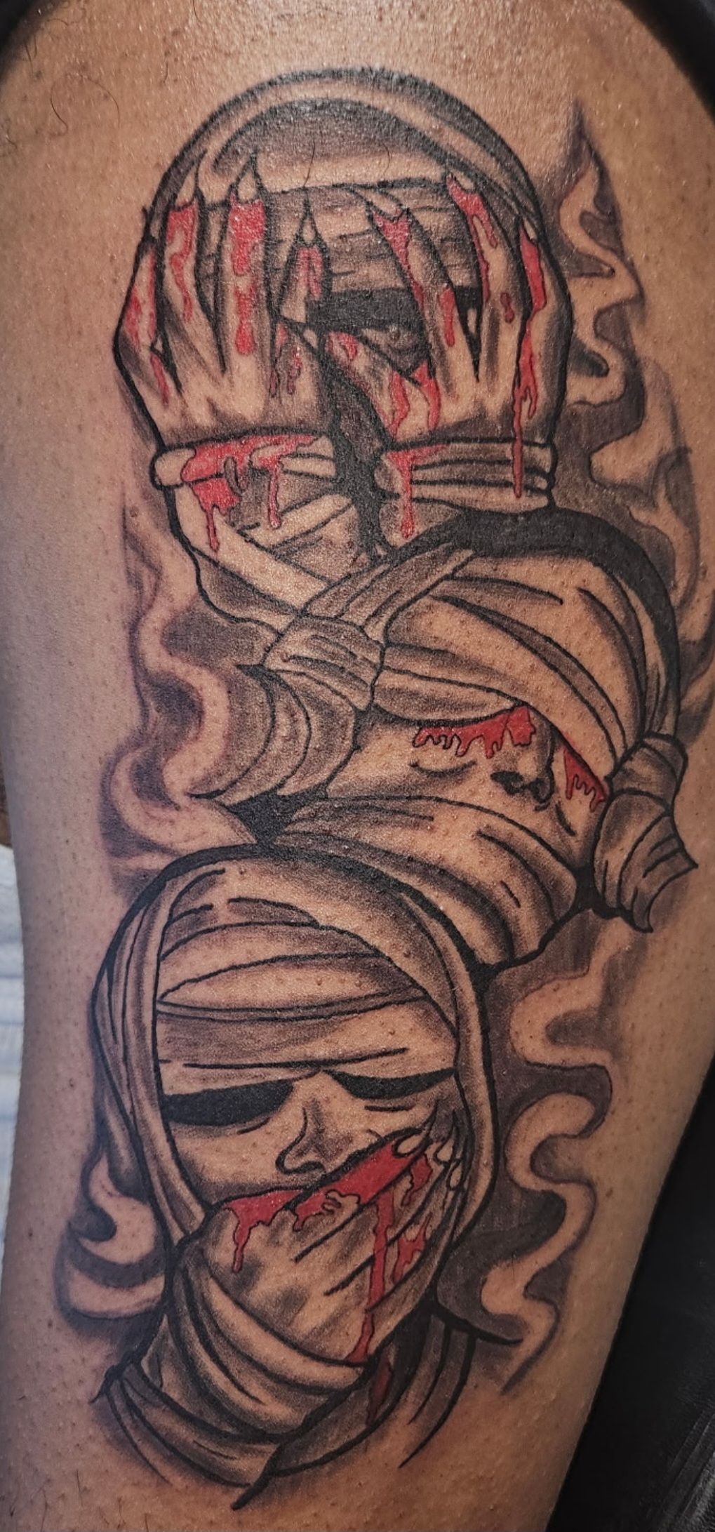 Black-and-gray tattoo of a scarred, wrapped mummy with red accents on skin