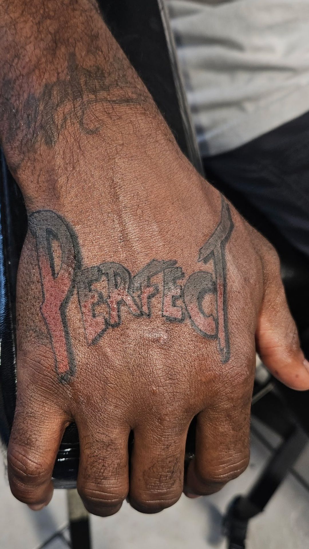 Close-up of a hand with a black tattoo across the back, resting against a light shirt.