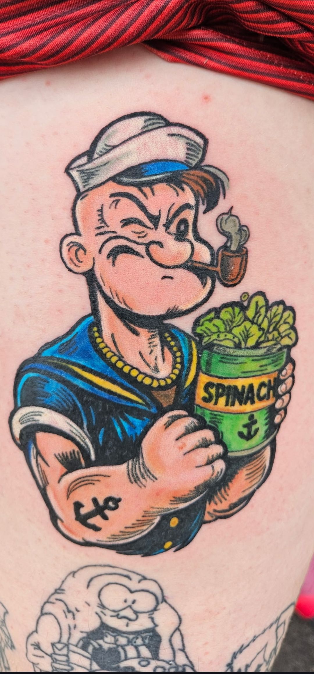 Cartoon Popeye tattoo holding a can of spinach, outlined in blue and black with red hair above.